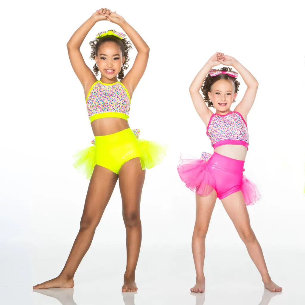 Two young dancers in colorful costumes pose with raised arms.