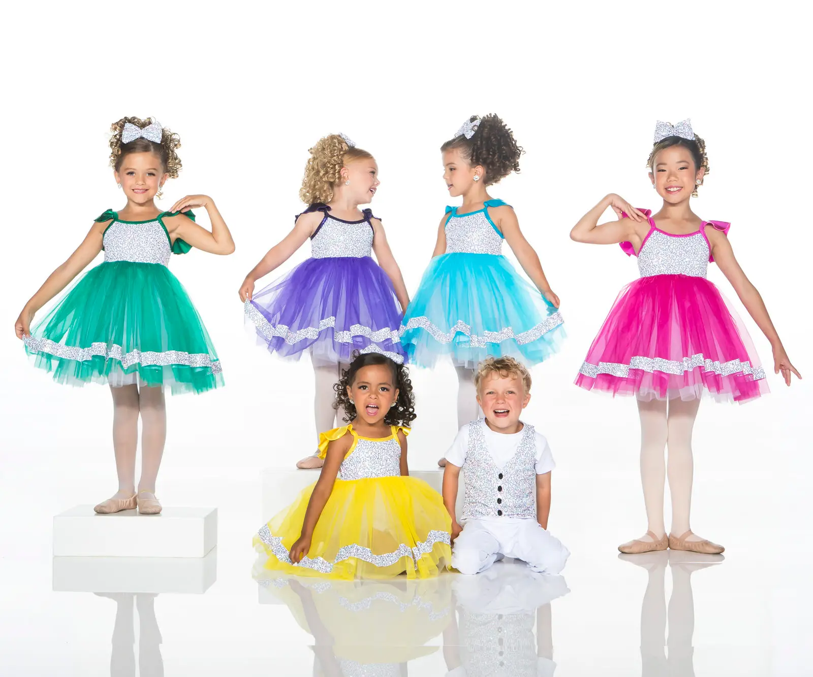 Children modeling colorful dance costumes against a white studio background