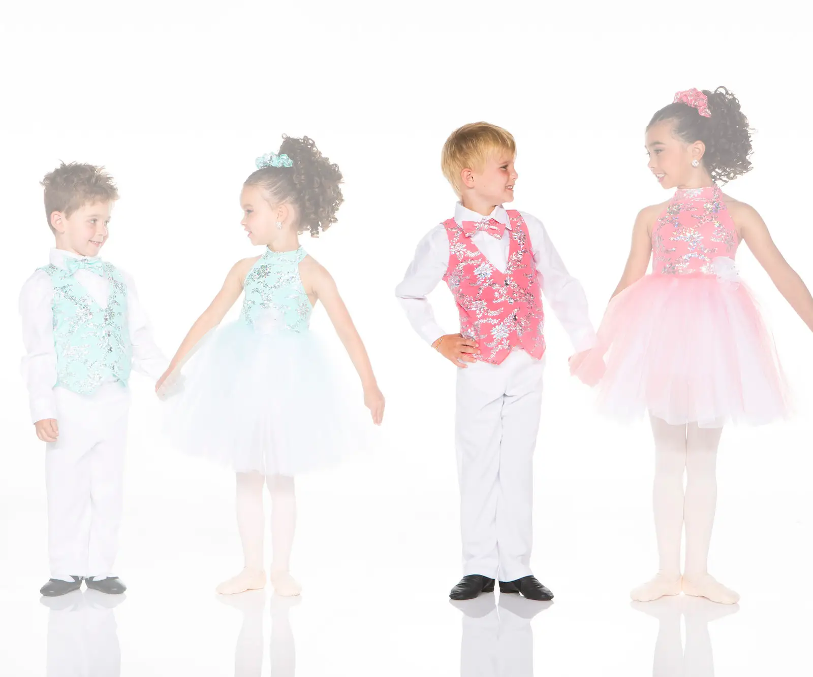 Four children in colorful ballroom dance costumes smiling together