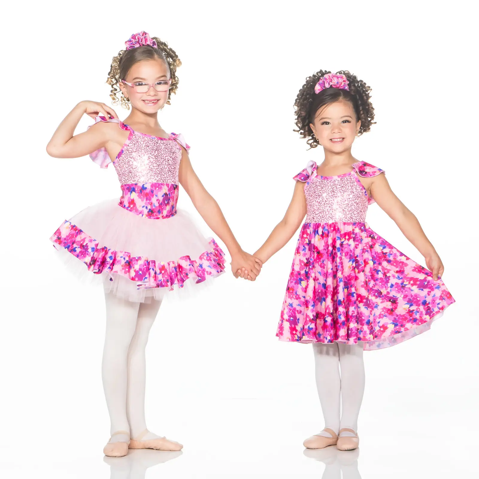 Two young dancers holding hands in pink floral costumes