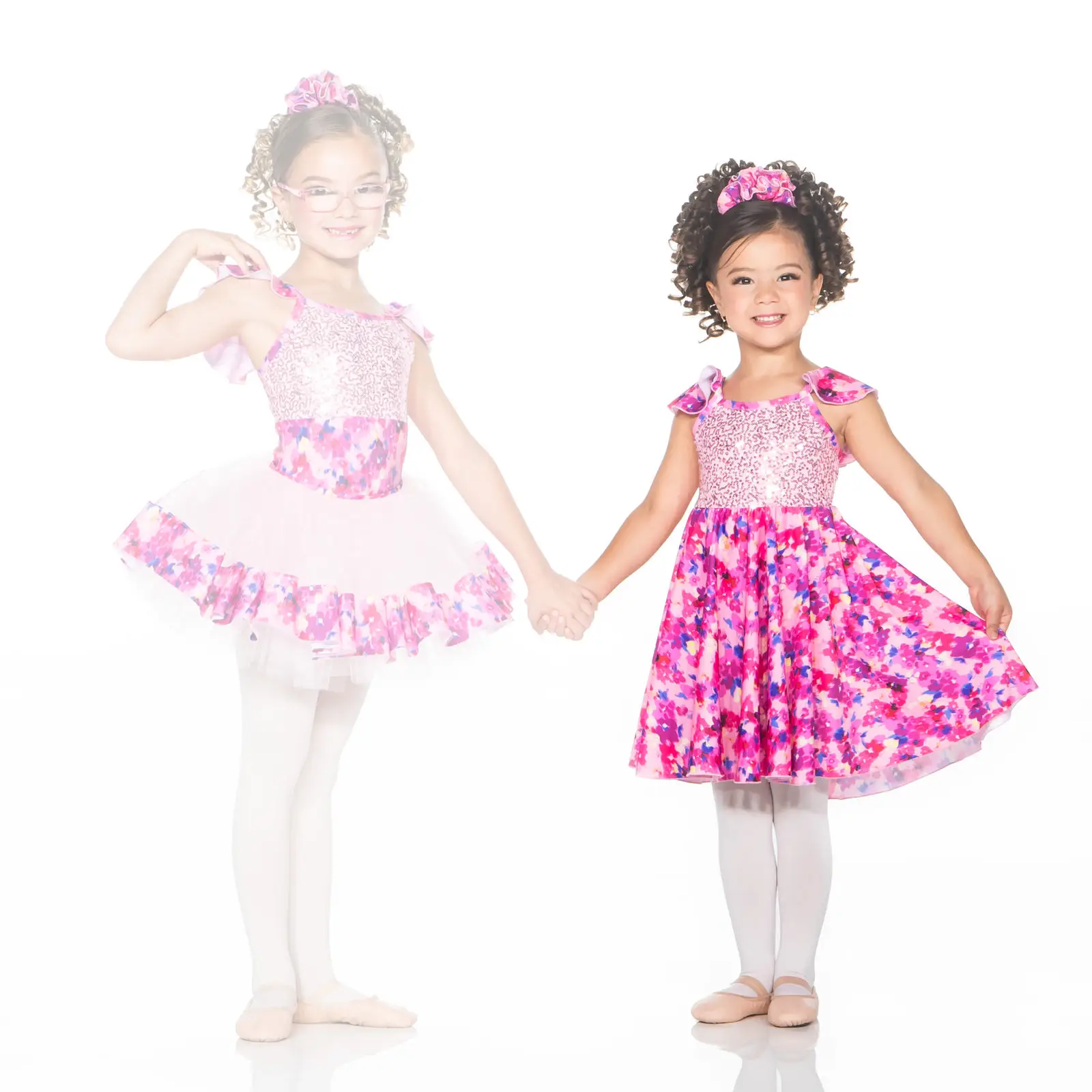 Two young girls in pink floral dance costumes holding hands