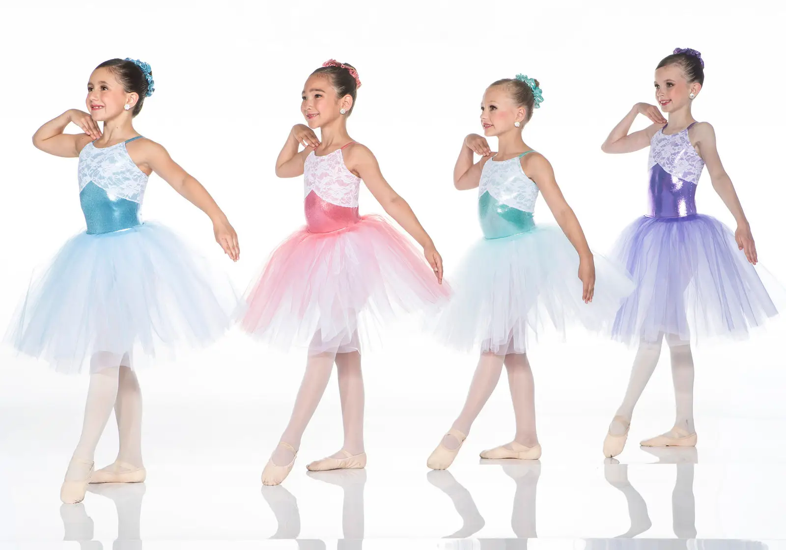 Four young ballerinas in colorful tutus posing against white background.
