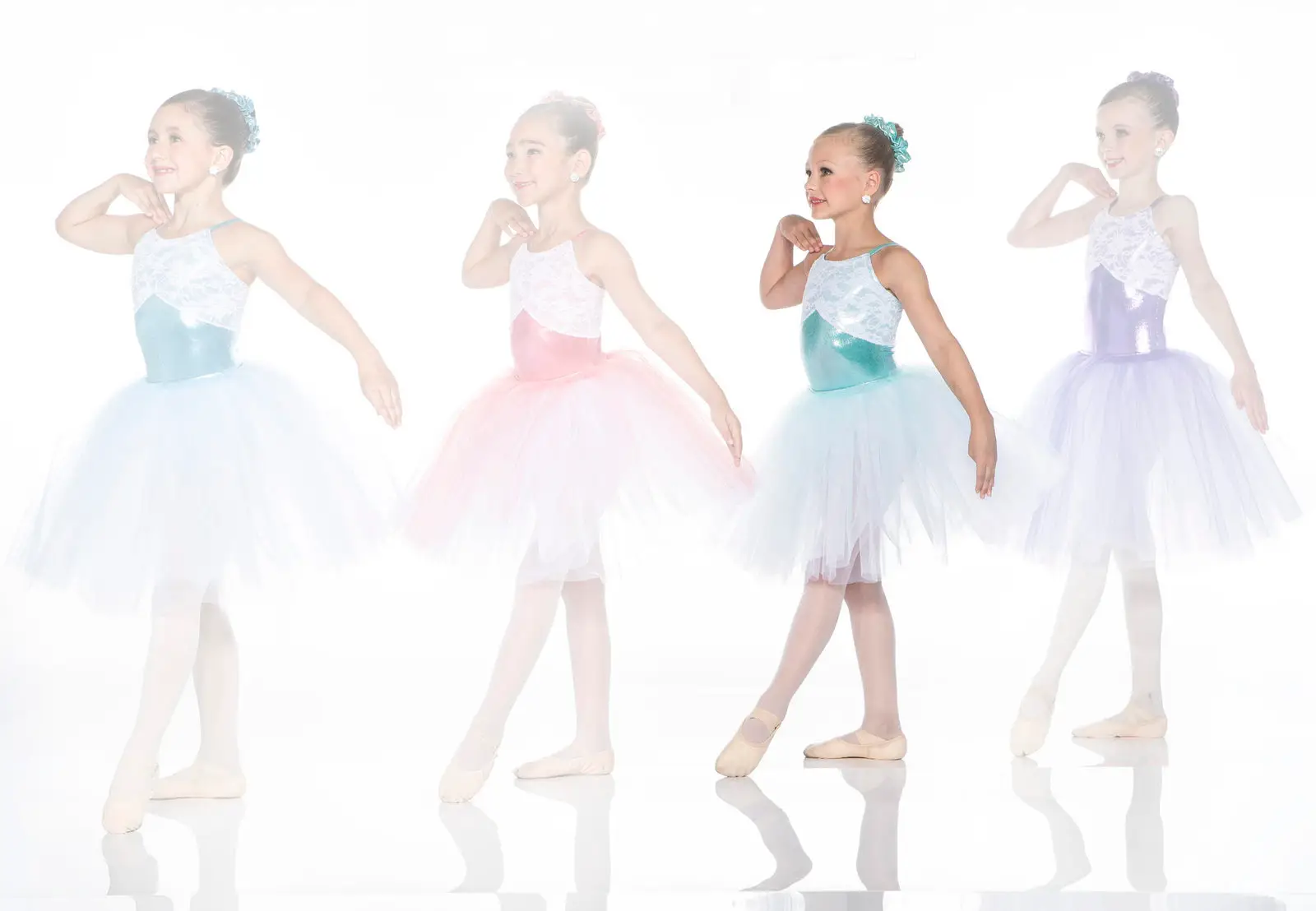 Four young ballerinas in pastel tutus pose against white background.