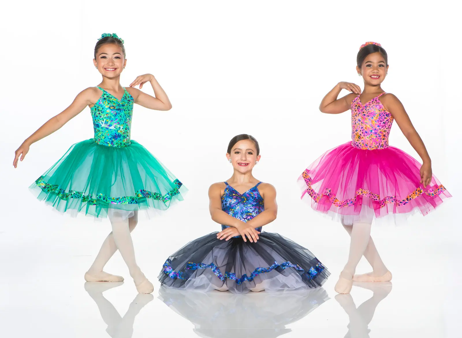 Three young ballet dancers in colorful tutus posing