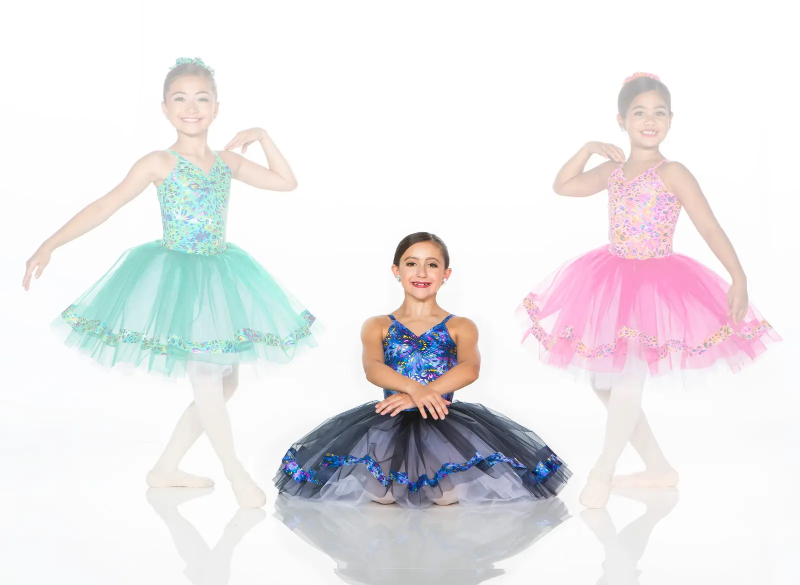 Three young ballerinas wearing colorful tutus against a white background.