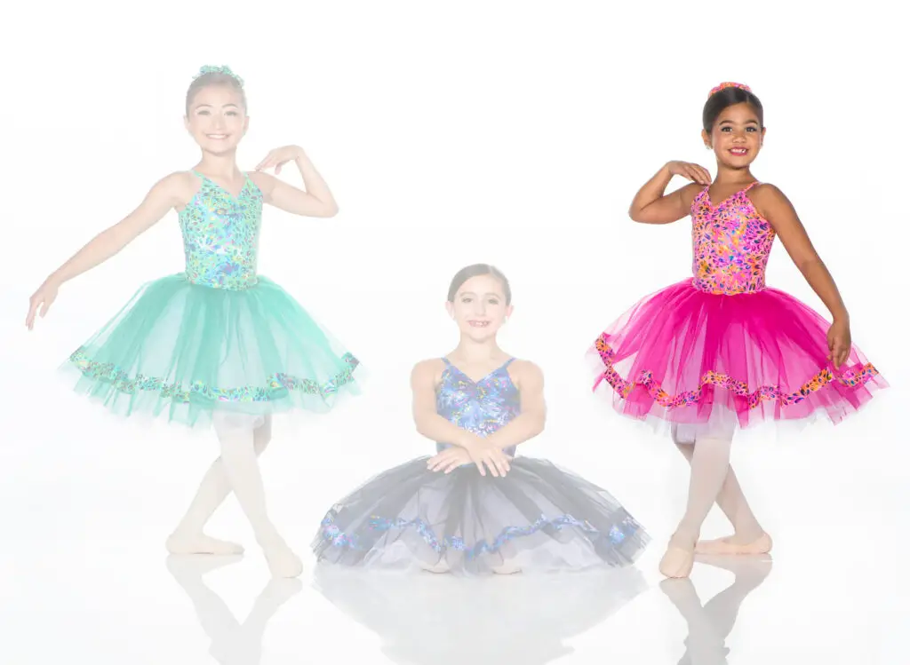 Three young ballet dancers wearing colorful tutus pose together.