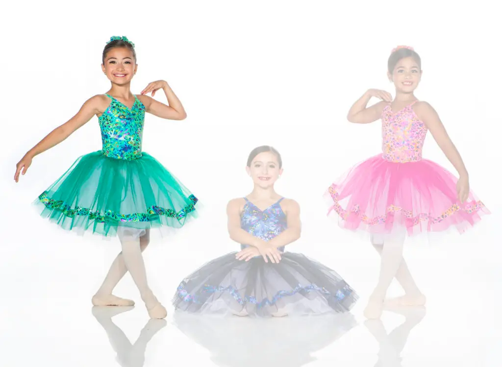 Three young ballet dancers wearing colorful tutus against white background