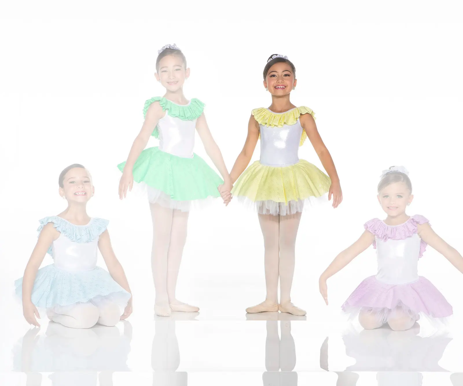 Four young ballerinas wearing pastel ruffled tutus pose together