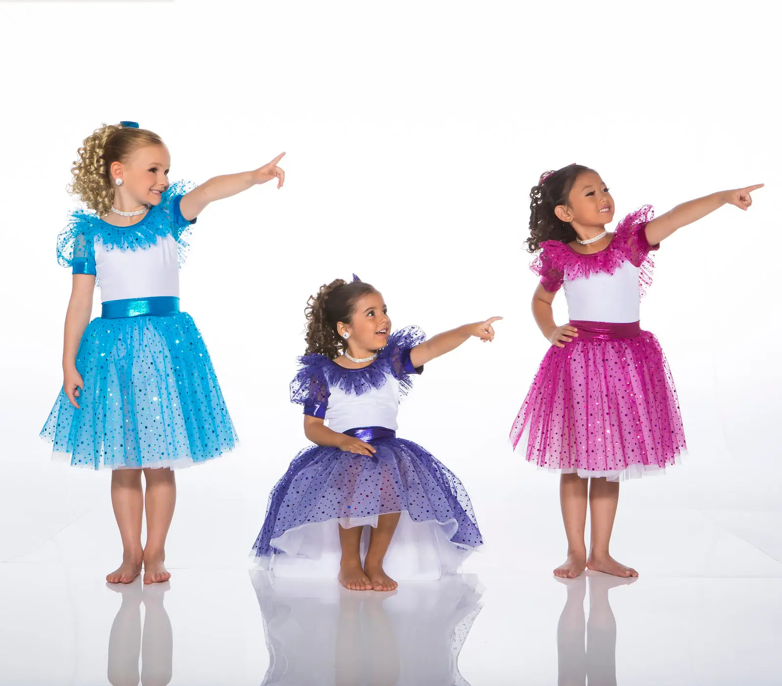 Three girls in colorful dance dresses pointing right