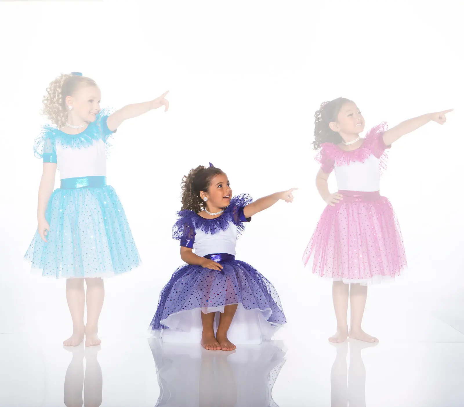 Three girls in colorful dresses point to the right.