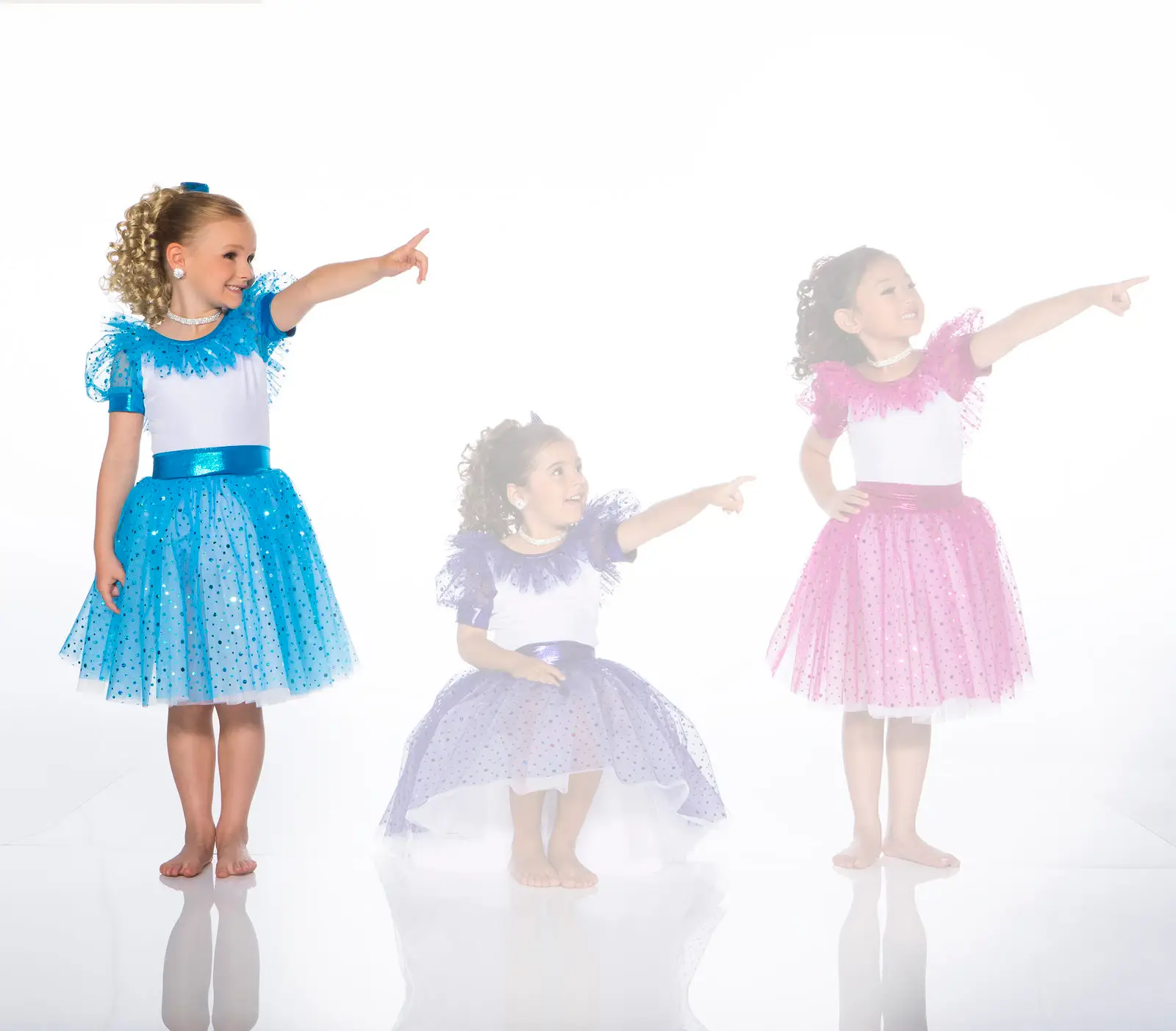 Three girls in colorful dance costumes pointing right