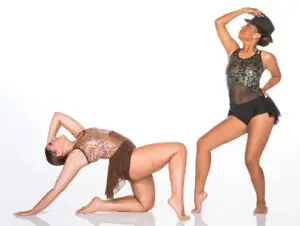 Two dancers posing in sequined costumes against white background.