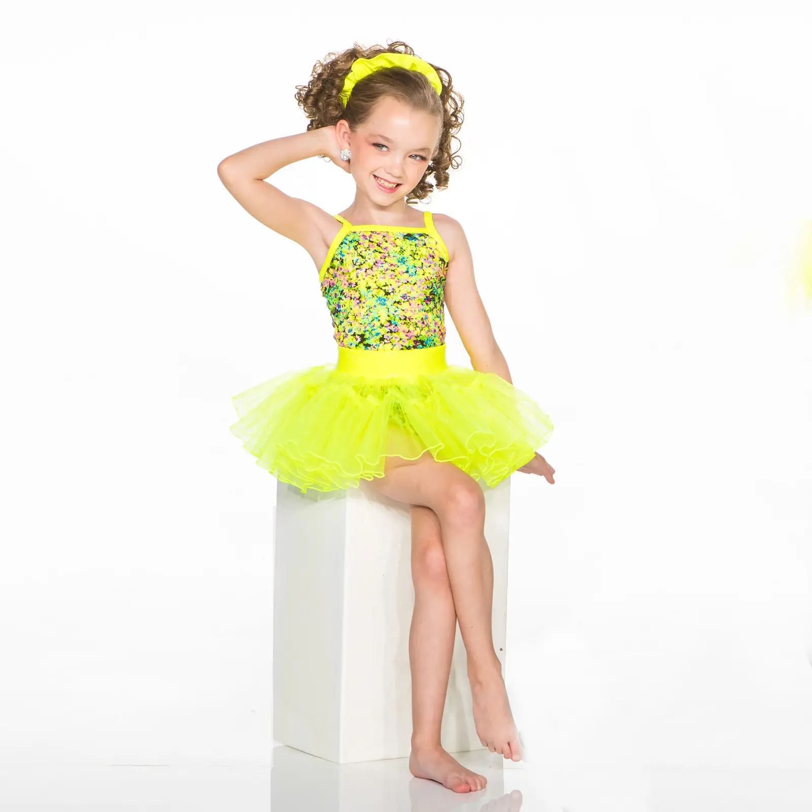 Smiling young dancer in neon yellow tutu seated on pedestal