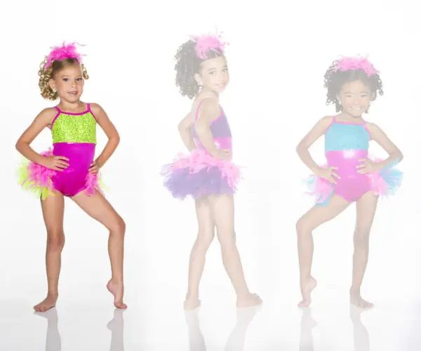 Three young dancers wearing colorful feathered costumes pose.