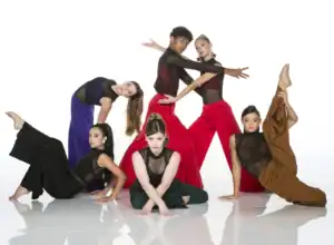 Six dancers pose dramatically in colorful costumes against white backdrop.