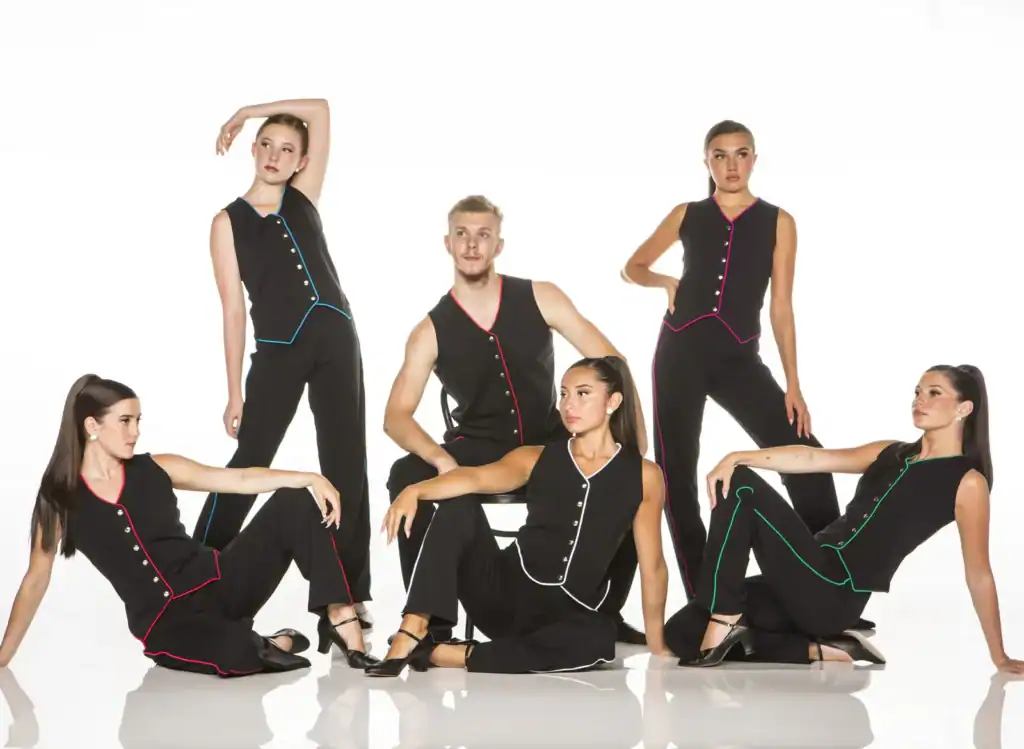Six dancers pose in black outfits with colorful trim.