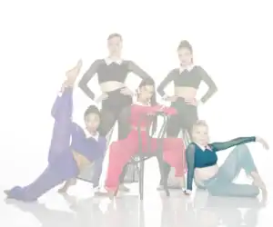 Five dancers pose in colorful costumes around a chair.