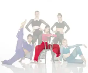 Five dancers pose in colorful costumes around a chair.