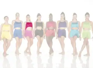 Seven dancers wearing colorful fringe costumes stand in a row.