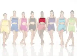 Eight dancers wearing colorful fringed costumes stand in a row.