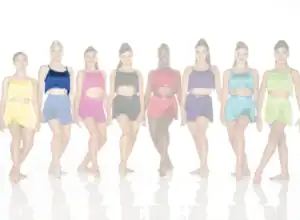 Eight dancers wearing colorful fringed costumes stand in a row.