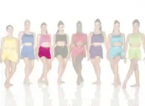 Eight dancers wearing colorful fringe costumes stand in a row.