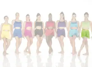 Eight dancers wearing colorful fringed costumes stand in a row.