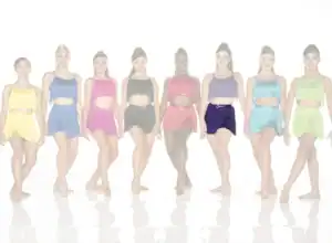 Seven dancers wearing colorful fringed costumes pose in a row.