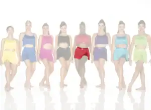 Eight dancers wearing colorful fringe costumes stand in a row.