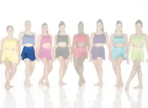 Seven dancers wearing colorful fringe costumes against a white background