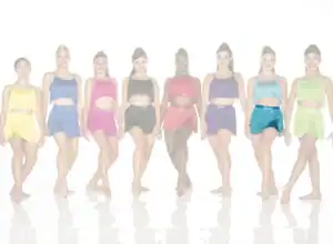 Eight dancers wearing colorful fringed costumes stand in a row.