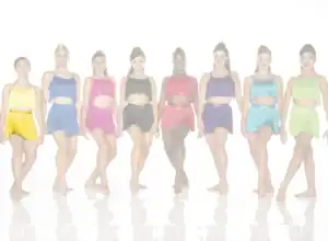 Seven dancers wear colorful fringe costumes against a white background.