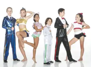 Six young dancers pose in colorful costumes against white background.