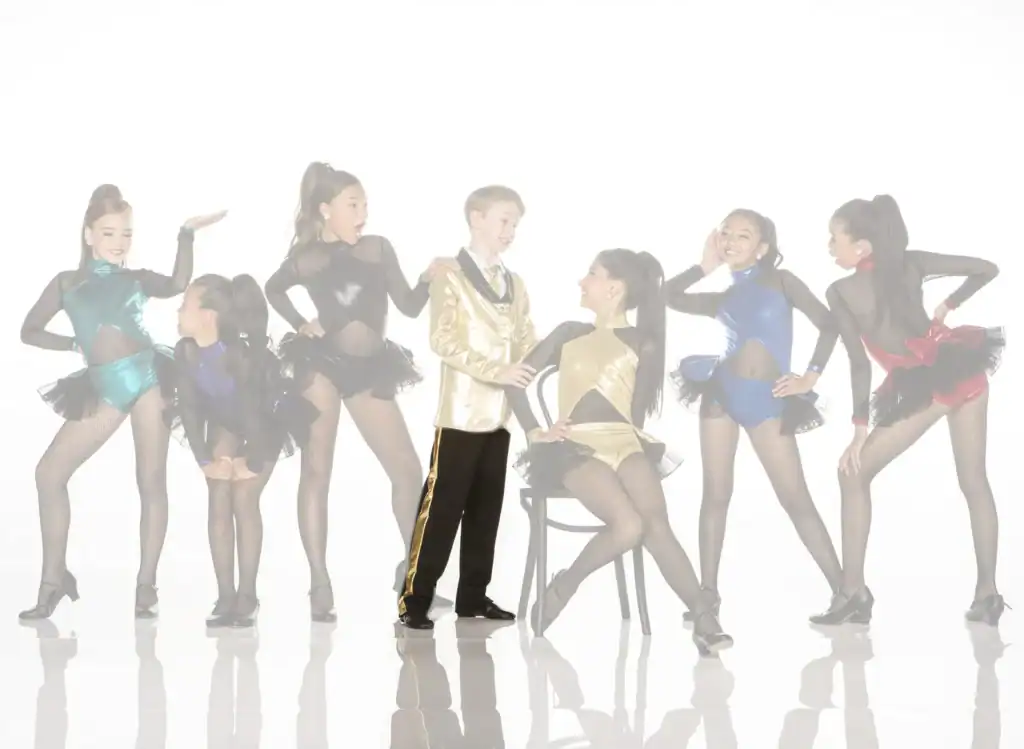Young dancers in colorful costumes pose with boy in gold jacket.