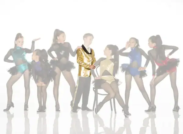 Young dancers pose in colorful costumes around boy in gold jacket