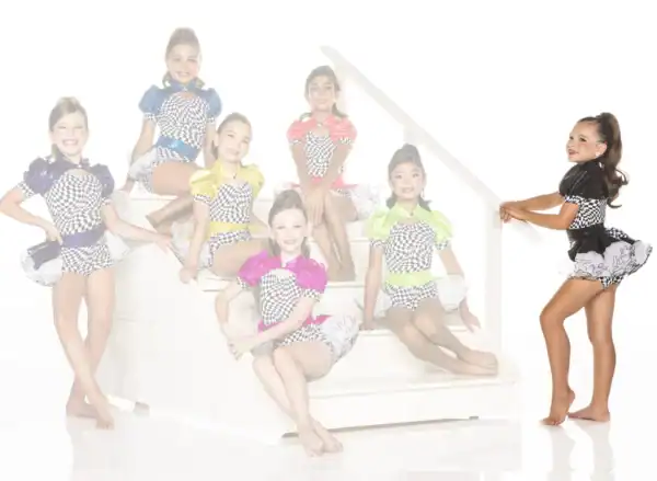 Seven young dancers in colorful checkered costumes posing on stairs
