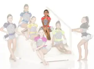 Seven young dancers in colorful checkered costumes pose on stairs.