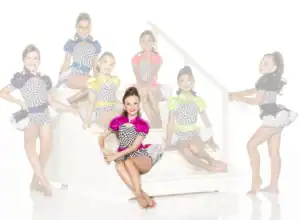 Seven young dancers in colorful checkered costumes posing on stairs.