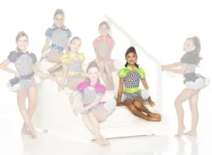 Seven young dancers in colorful checkered costumes on white stairs
