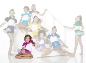 Seven young dancers in colorful costumes pose on white stairs.