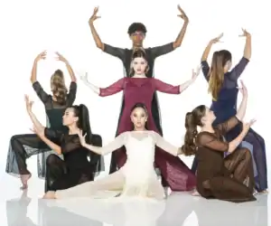 Six dancers pose in colorful sheer costumes against white backdrop.