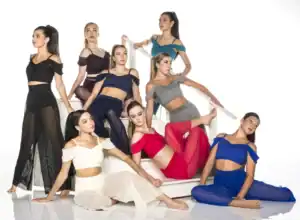 Eight dancers in colorful outfits posing on white stairs