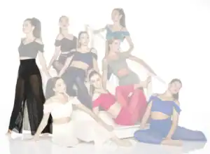 Eight dancers pose on a white staircase in colorful outfits.