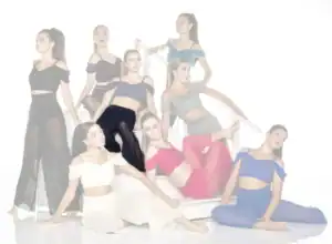 Nine women pose in colorful dance outfits on white stairs.