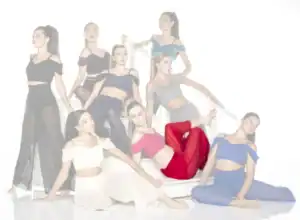 Nine women pose in colorful outfits on white stairs.