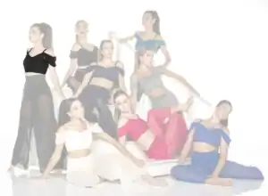 Eight dancers in colorful outfits pose on a white staircase.