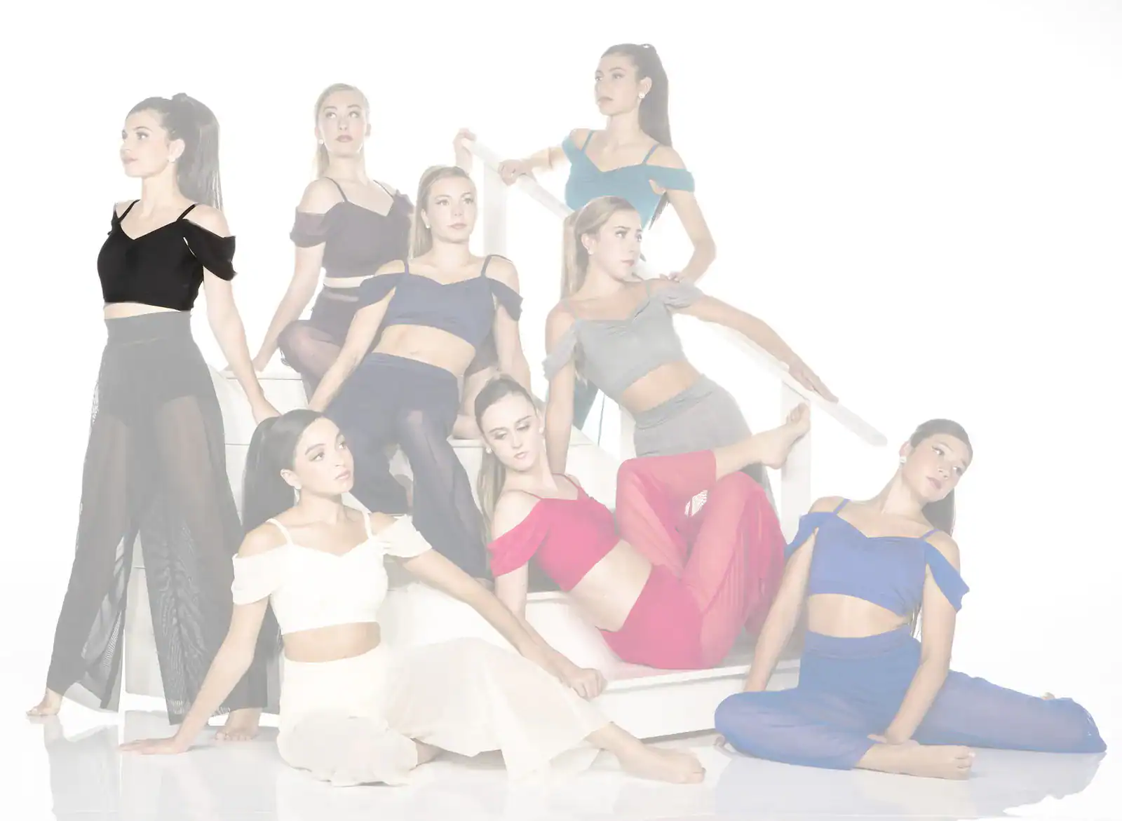 Eight dancers in colorful outfits pose on a white staircase.