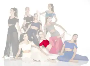 Eight dancers pose on white stairs in colorful outfits.