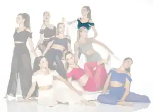 Eight women pose in colorful outfits on white stairs.