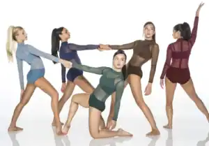 Five dancers pose in colorful sheer leotards against white backdrop.